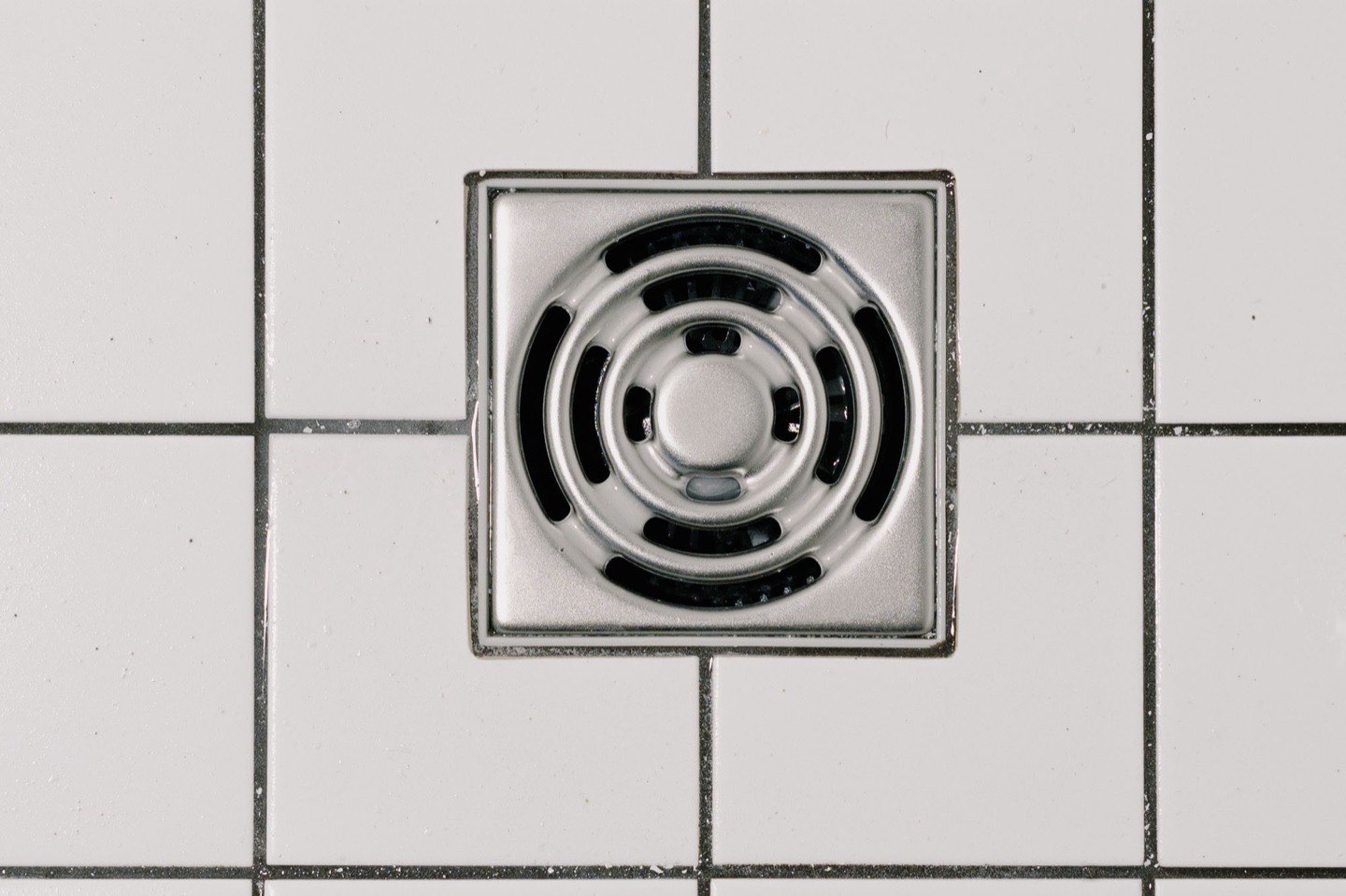 A stainless steel floor drain set into white tile