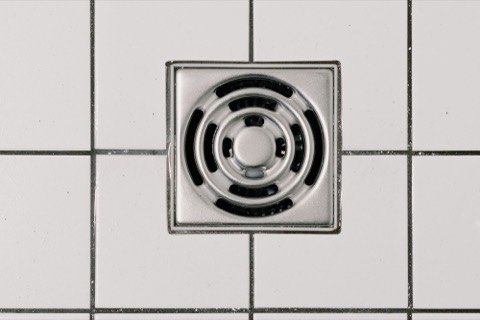 A stainless steel floor drain set into white tile