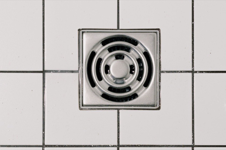 A stainless steel floor drain set into white tile