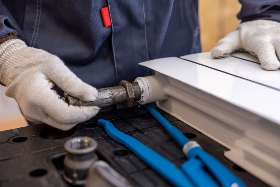 A plumber in work gloves fitting a threaded pipe connection